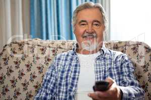 Portrait of smiling senior man operating remote while sitting on sofa