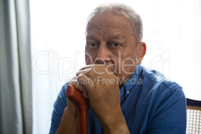 Portrait of sad senior man holding walking cane while sitting on chair