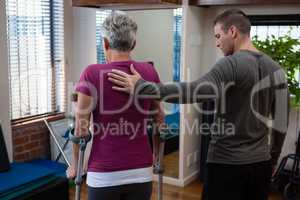 Physiotherapist assisting senior woman patient to walk with crutches