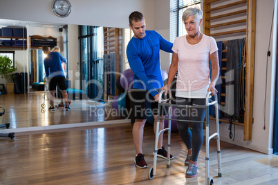 Physiotherapist assisting senior woman patient to walk with walking frame