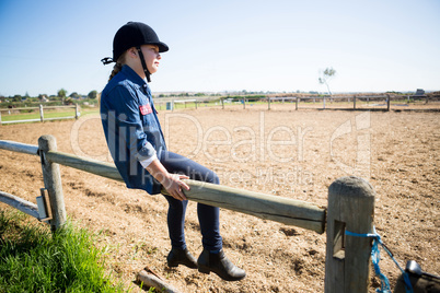 Girl sitting on wooden fence in the ranch