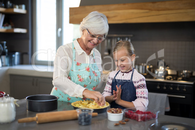 Grandmother and granddaughter adding fresh cut apples to the crust