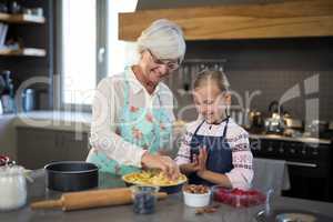 Grandmother and granddaughter adding fresh cut apples to the crust