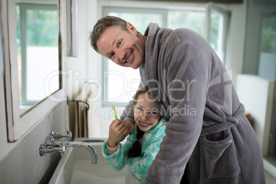 Smiling father and daughter holding toothbrush in bathroom