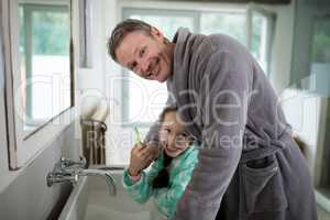 Smiling father and daughter holding toothbrush in bathroom