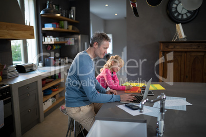 Father using a laptop while daughter is coloring