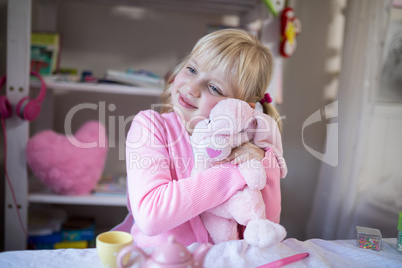 Smiling girl playing with a teddy bear and toy kitchen set