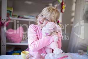 Smiling girl playing with a teddy bear and toy kitchen set