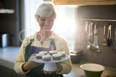 Senior women holding a tray of cupcakes in the kitchen