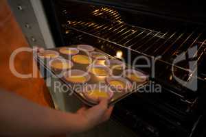 Cropped hands of girl keeping muffin tin in oven