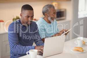 Father and son using laptop and digital tablet in kitchen