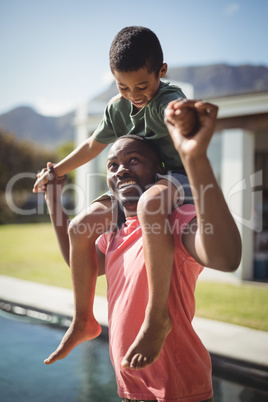 Father carrying son on shoulders near poolside