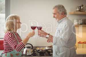 Senior couple toasting glasses of wine while preparing food