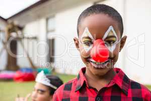 Portrait of boy with face paint wearing clown nose