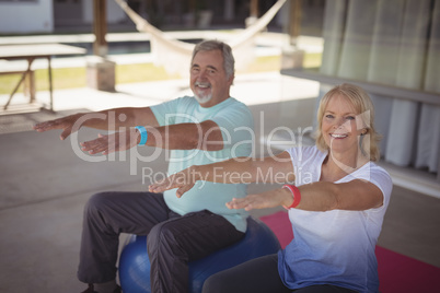 Smiling senior couple exercising on exercise ball