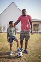 Smiling father and son standing in garden with football