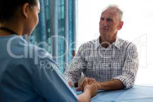 Doctor holding hands of senior man while consoling at nursing home