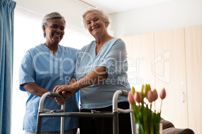 Nurse standing by senior woman holding walker in nursing home