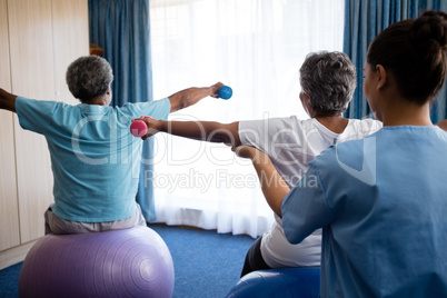 Rear view of nurse training seniors in lifting dumbbells