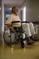 Thoughtful senior man sitting on wheelchair in corridor