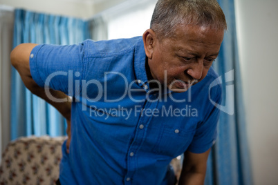 senior man holding back while standing in nursing home