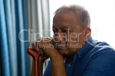 Thoughtful senior man with walking cane sitting by window in nursing home