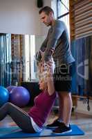 Male physiotherapist helping girl patient in performing stretching exercise on exercise mat