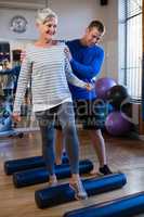 Physiotherapist assisting senior woman in performing exercise on foam roll