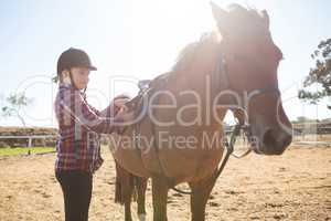 Girl adjusting saddle on horse in ranch
