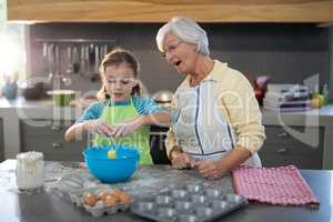 Granddaughter breaking eggs and grandmother watching