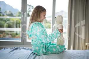 Smiling girl holding teddy bear on bed in bedroom