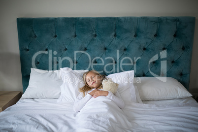 Girl sleeping on bed with teddy bear in bedroom