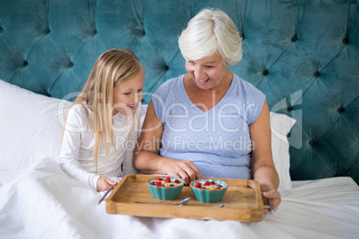 Smiling granddaughter and grandmother having breakfast on bed