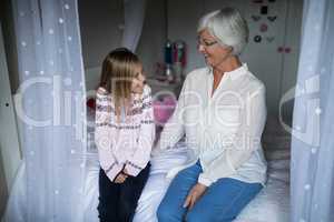Smiling grandmother and granddaughter interacting with each other on bed