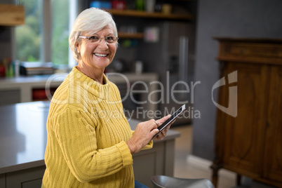 Senior women holding a tablet while standing in the kitchen