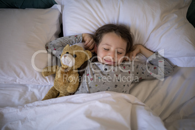 Girl sleeping on bed with teddy bear in bedroom