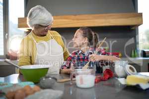 Granddaughter mixing flour in a bowl while looking at grandmother