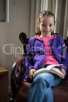 Smiling girl reading book on chair in living room