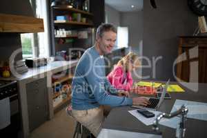Father using a laptop while daughter is coloring