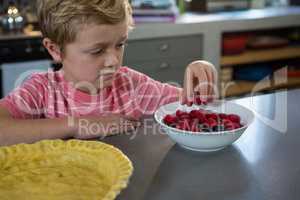 Boy having raspberries in kitchen