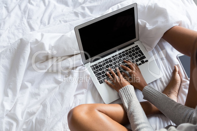 Low section of woman using laptop while relaxing on bed
