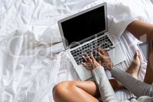 Low section of woman using laptop while relaxing on bed