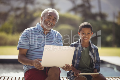 Smiling grandfather and grandson sitting together on bench with laptop and digital tablet