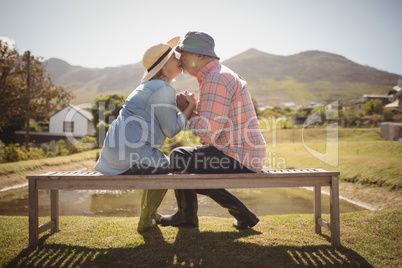 Senior couple kissing each other while sitting on a bench in lawn