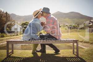 Senior couple kissing each other while sitting on a bench in lawn