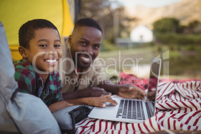 Smiling father and son using laptop in tent