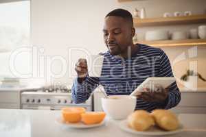 Man using a digital tablet while having cup of coffee in kitchen