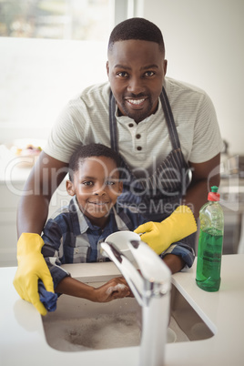 Smiling father and son cleaning utensils in kitchen