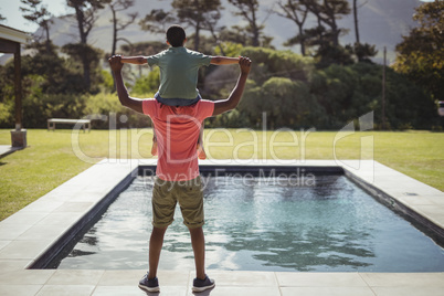 Father carrying son on shoulders near poolside