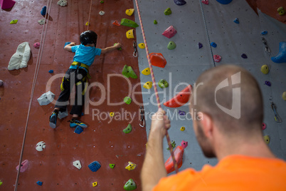 Trainer assisting boy in rock climbing